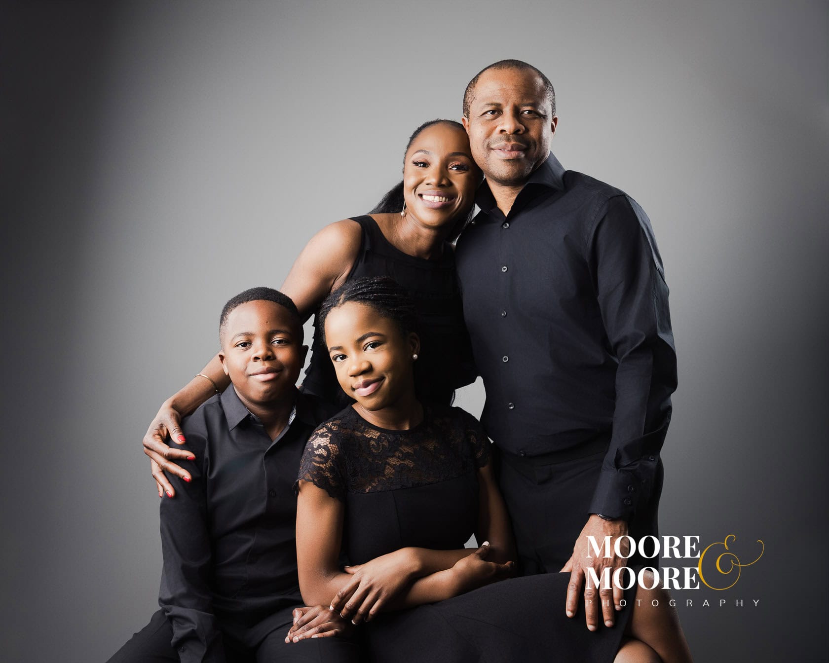 Family portrait of parents with two children dressed in black during a studio photography session at Moore & Moore Photography in Fleet, Hampshire.