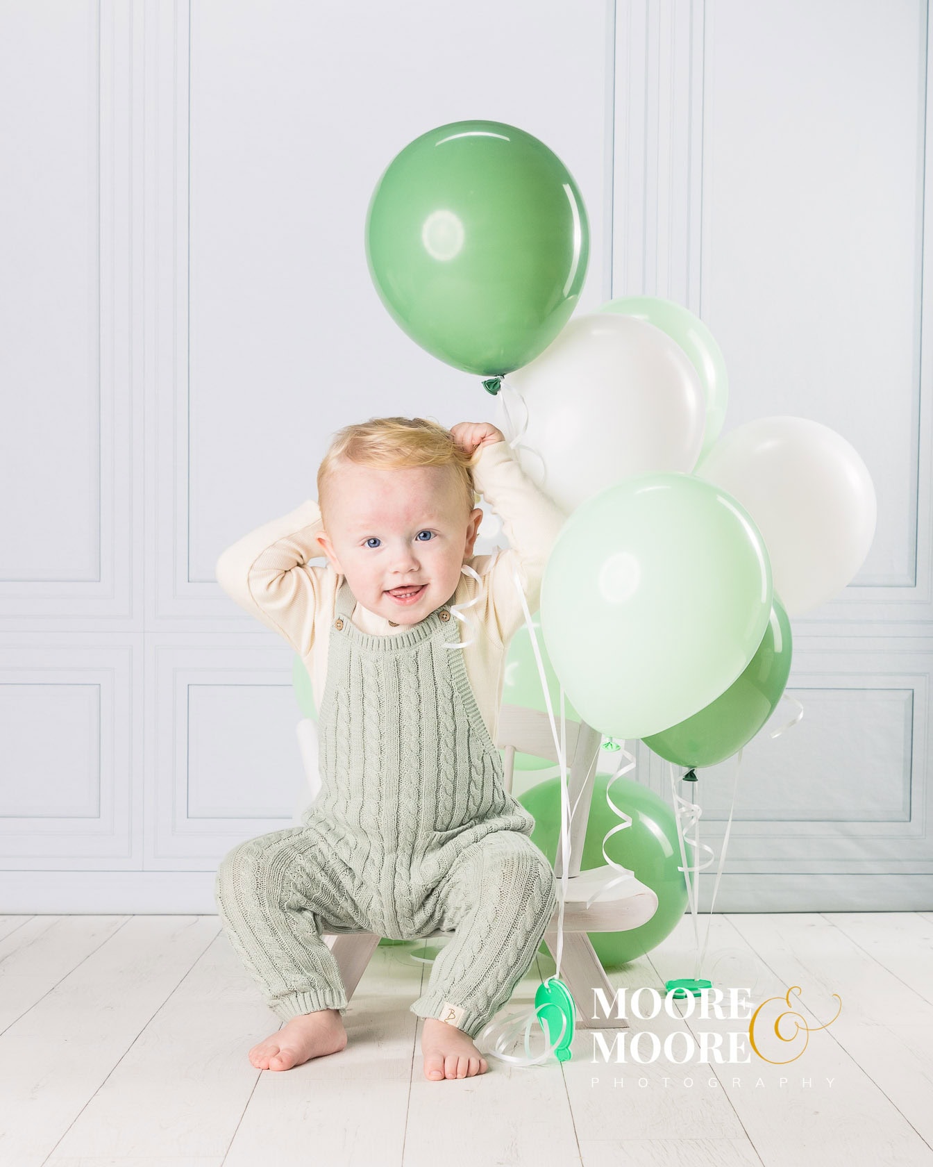 baby boy smiling with his green birthday balloons in a cosy home photographic studio