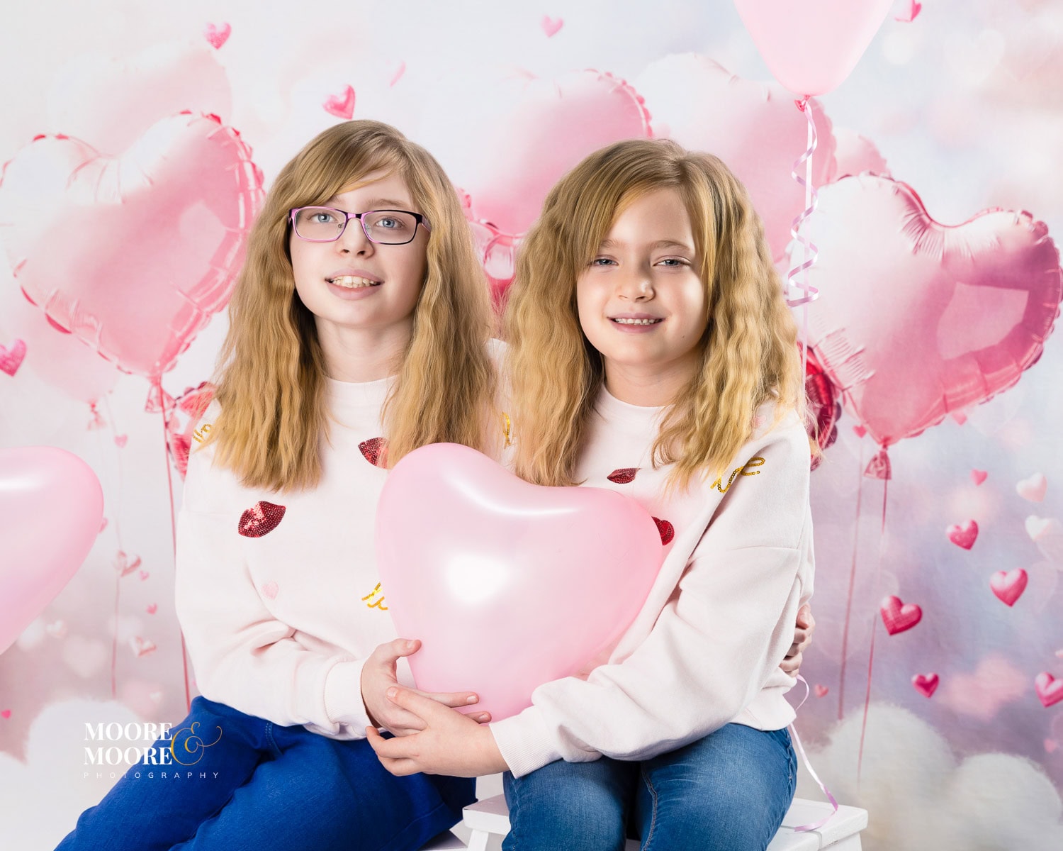 valentines-photo-experience-hampshire-11 Two sisters holding a pink heart balloon during a Valentine’s themed children’s portrait session at Moore & Moore Photography in Fleet, Hampshire.