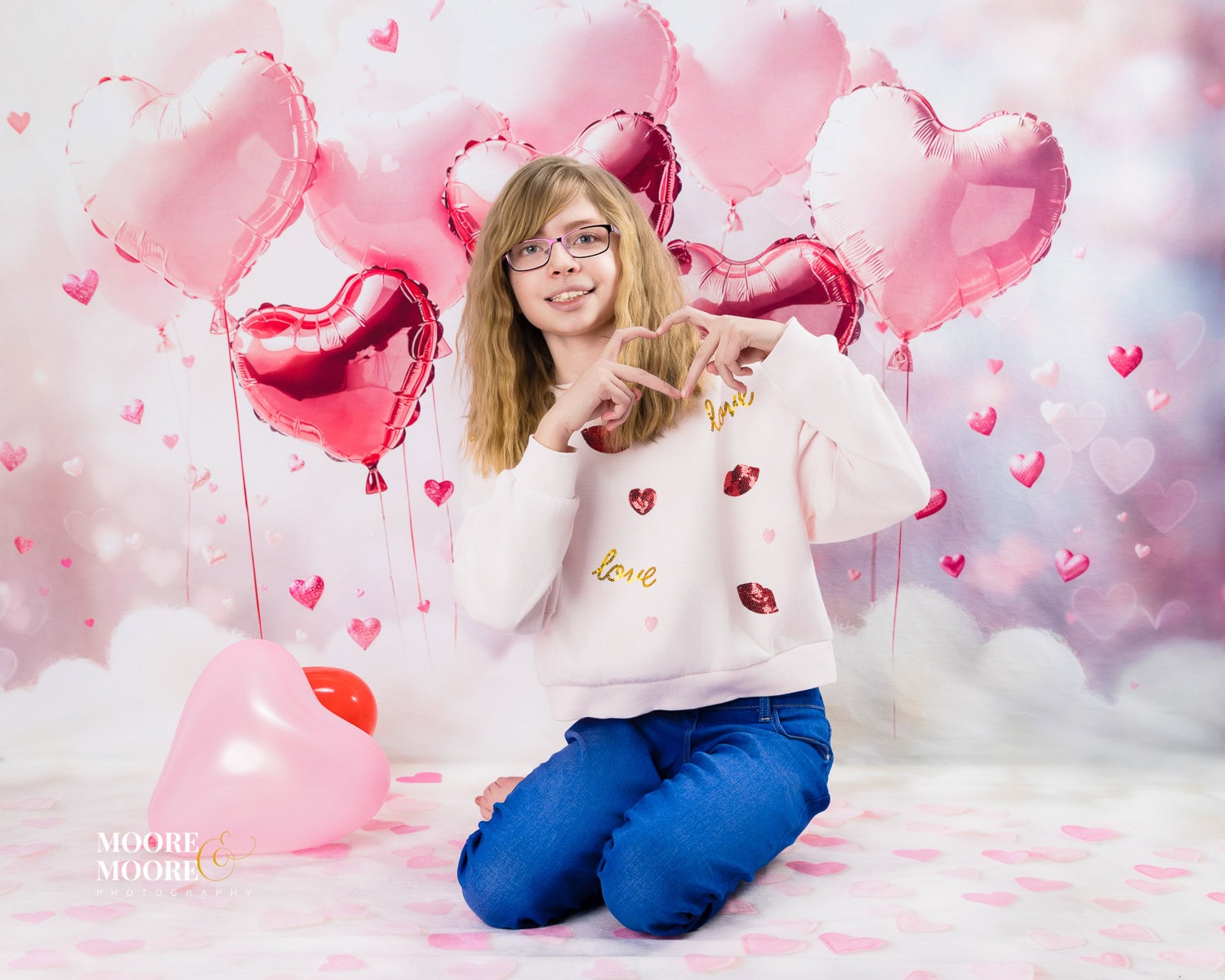 valentines-photo-experience-hampshire-12 Young girl kneeling in front of pink heart balloons during a Valentine’s themed children’s portrait session at Moore & Moore Photography in Fleet, Hampshire.