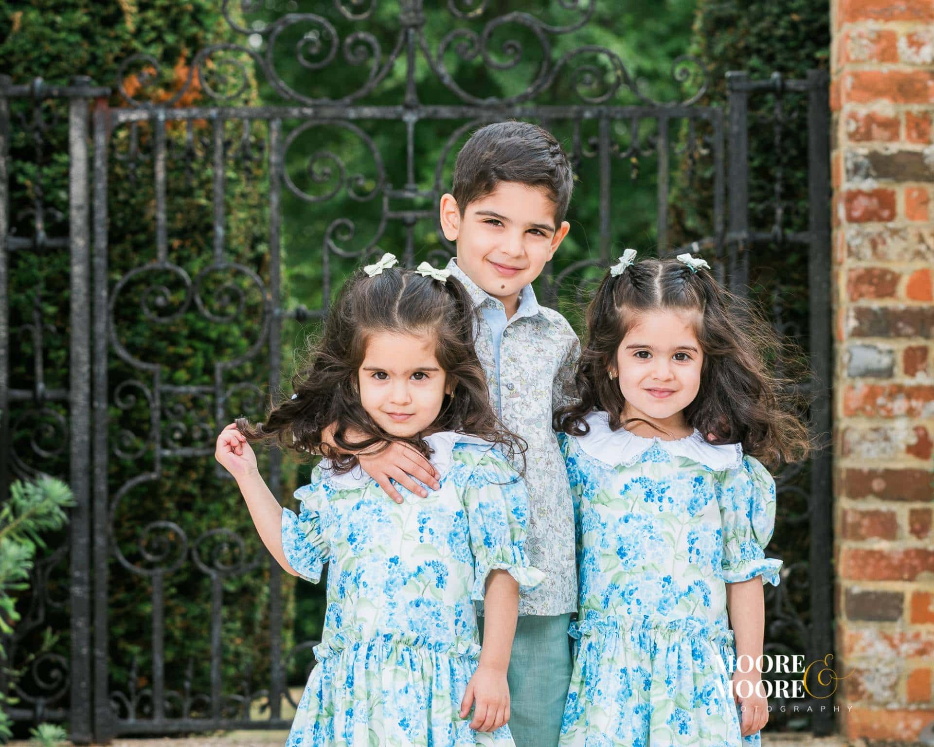 family-connection-portrait-hampshire-children Three siblings standing closely together outdoors, smiling naturally and showing connection and warmth during a relaxed family portrait in Hampshire.