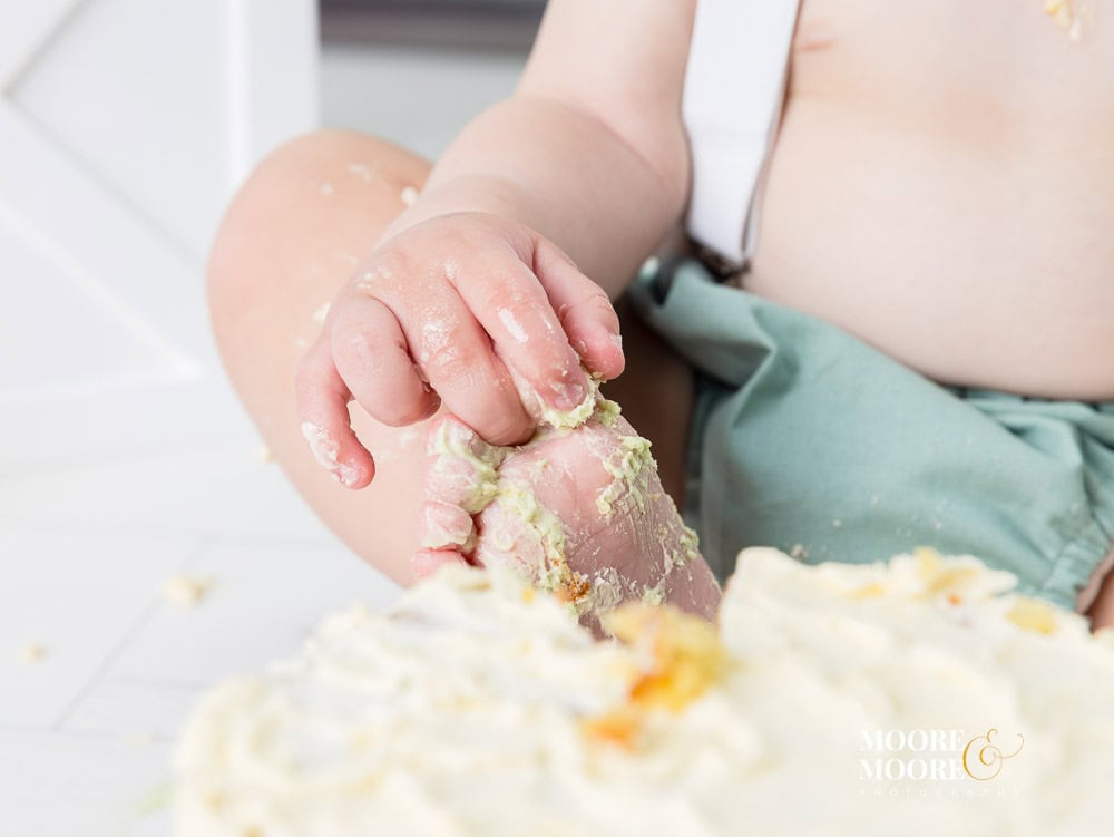 Close-up of a baby’s hands covered in birthday cake during a first birthday celebration, capturing the playful details of this milestone year.