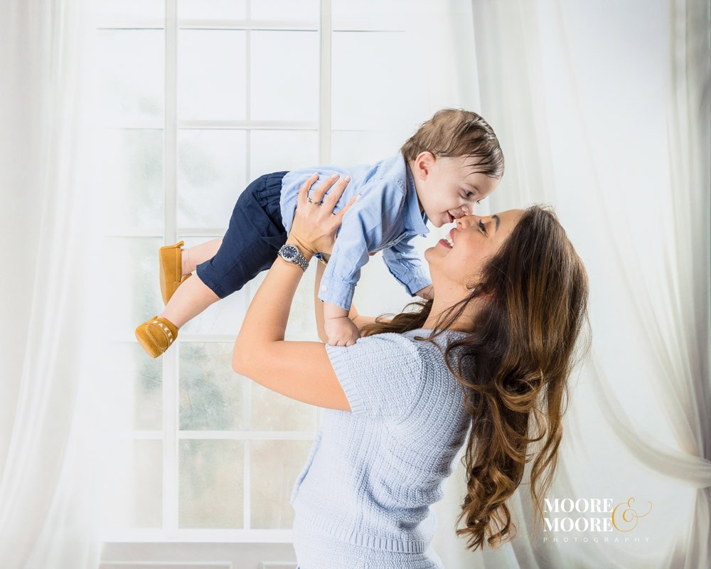 Mother lifting her baby into the air during a first birthday portrait, sharing a joyful and connected moment.
