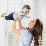 Mother lifting her baby in playful movement during a first birthday portrait session, capturing laughter and connection.