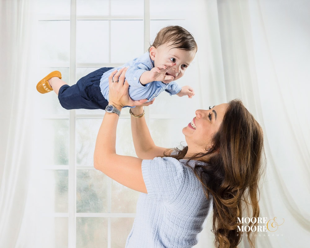 Mother lifting her baby in playful movement during a first birthday portrait session, capturing laughter and connection.