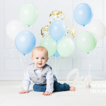 one year old baby sitting with pastel balloons celebrating first birthday milestone