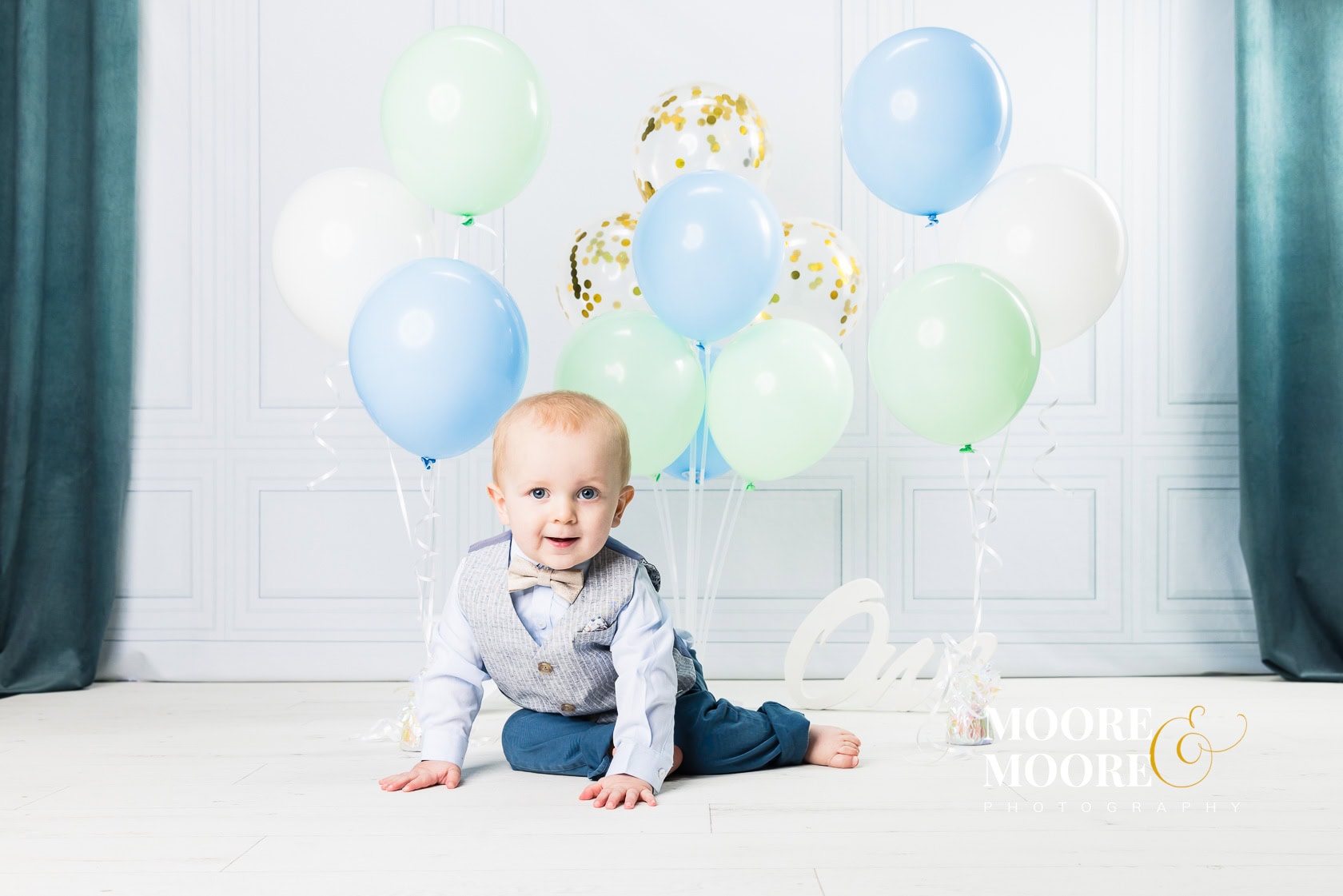 baby-laughing-during-first-birthday-celebration one year old baby sitting with pastel balloons celebrating first birthday milestone