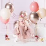 Smiling baby girl sitting with balloons during a relaxed first birthday portrait session in Fleet, Hampshire studio