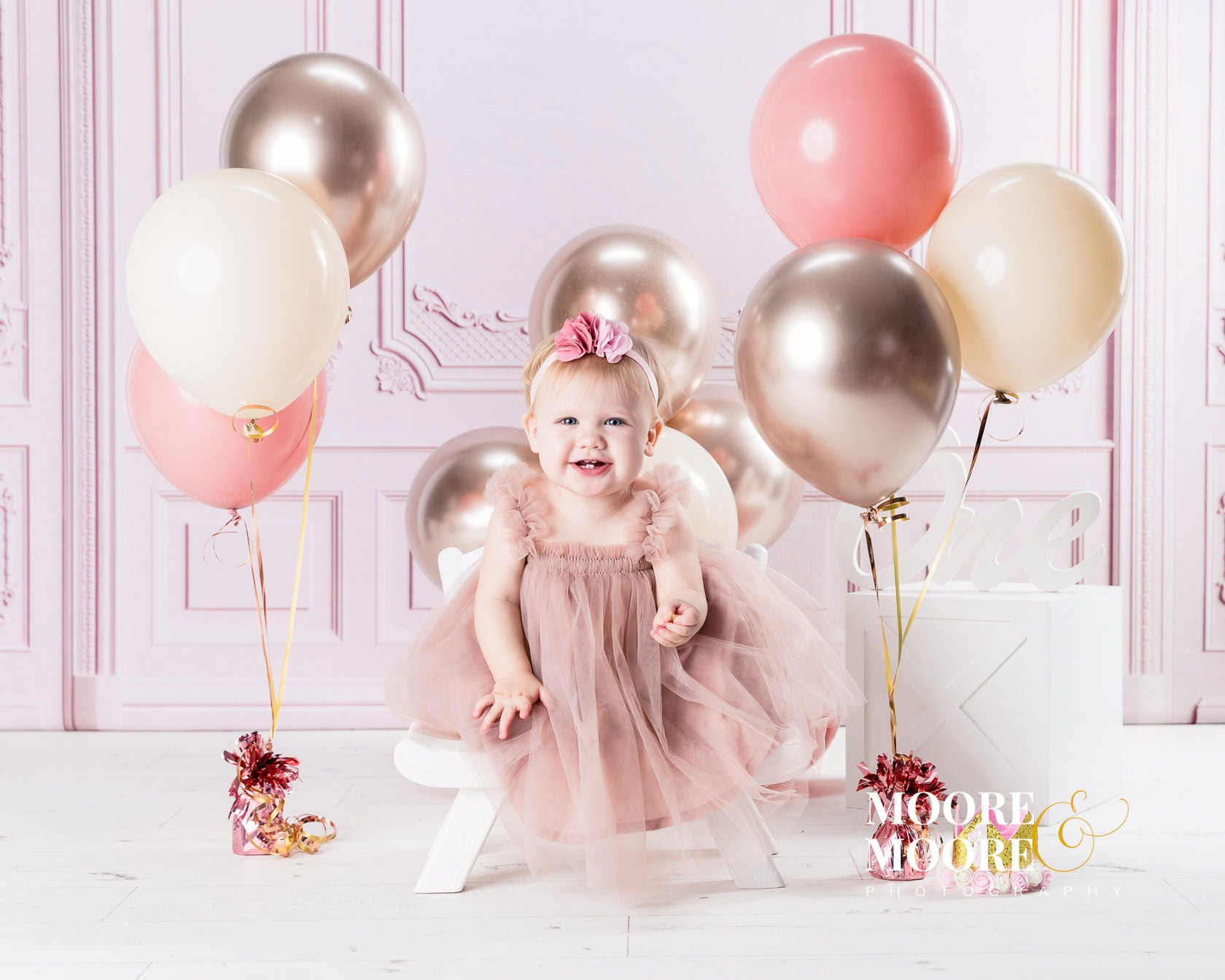 Smiling baby girl sitting with balloons during a relaxed first birthday portrait session in Fleet, Hampshire studio