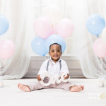 one year old baby sitting with pastel balloons holding one sign during first birthday portrait