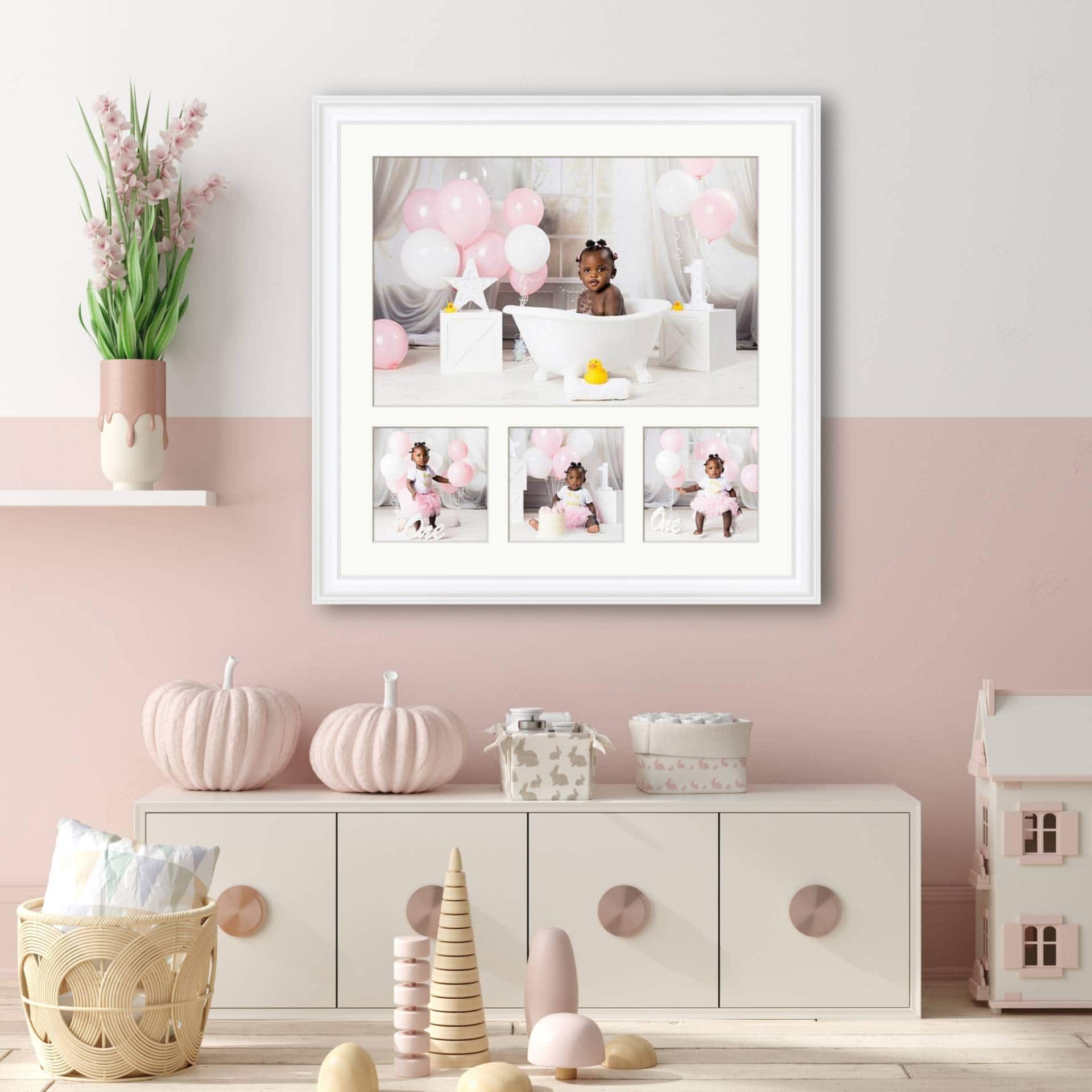 childrens-bedroom-first-birthday-framed-portrait-collection White-framed collection of four First Birthday portraits displayed above a low cabinet in a soft pink child's bedroom.