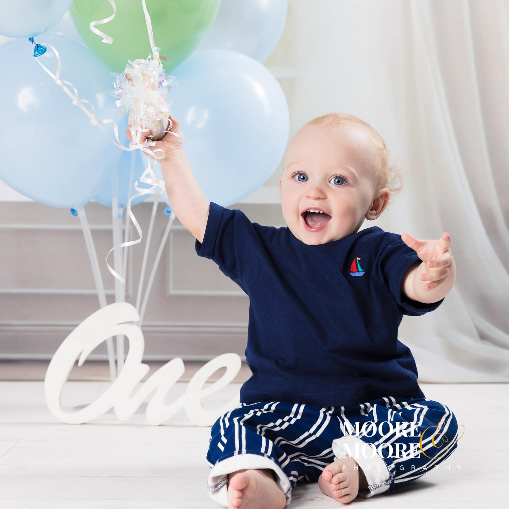 happy one year old baby reaching for balloons during a first birthday celebration